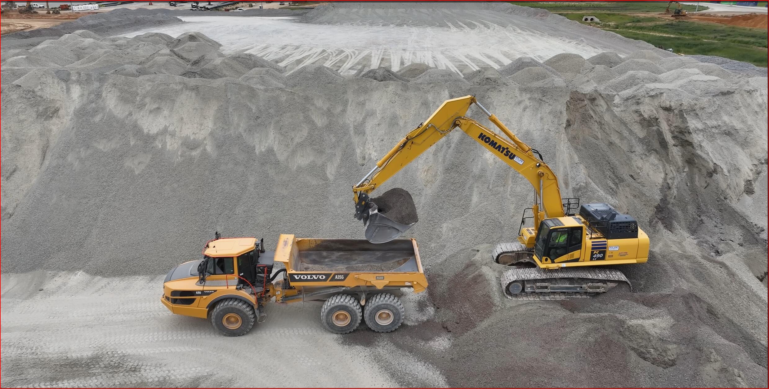 An excavator loading gravel into a dump truck at a construction site.