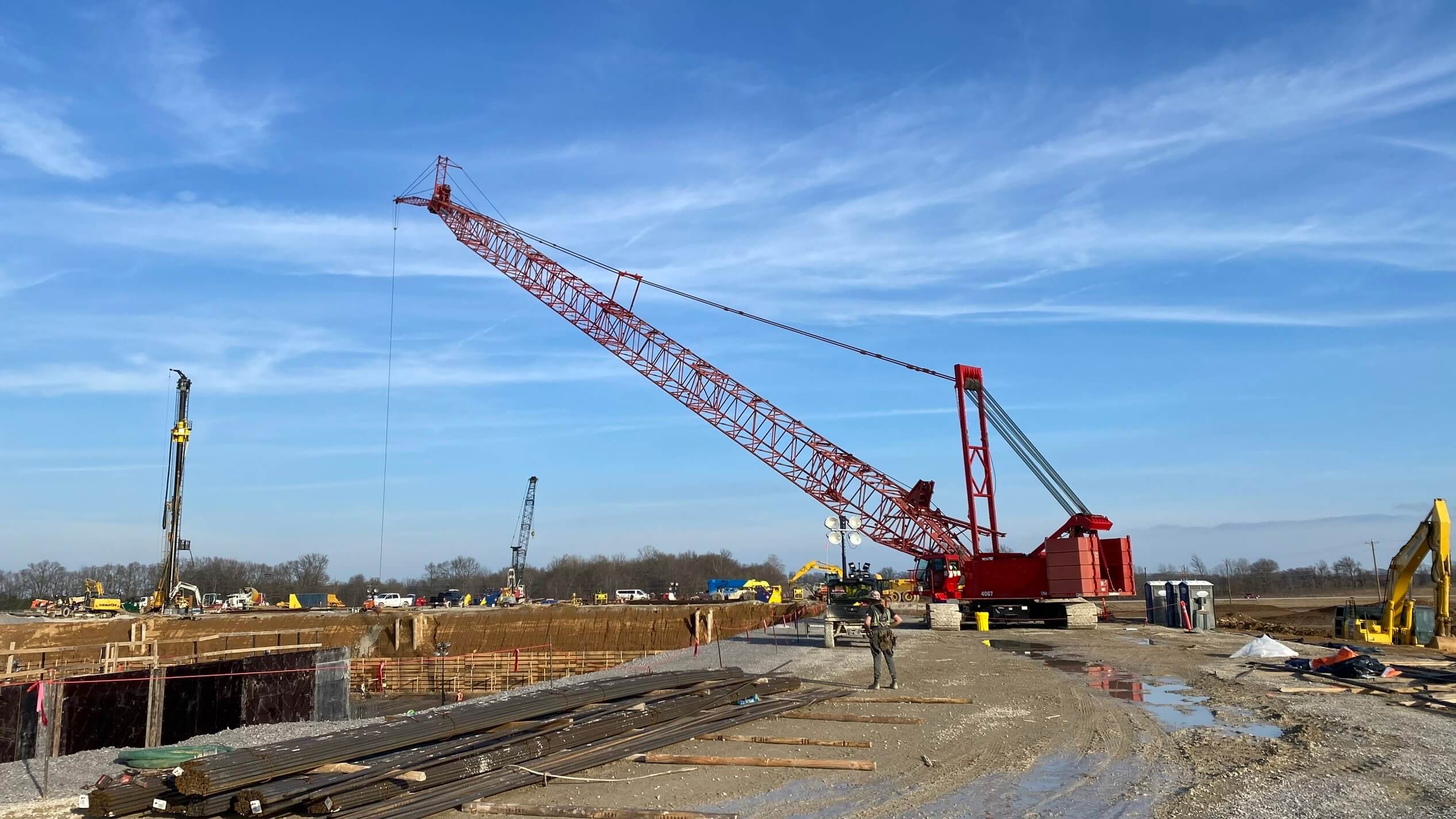 A large red crane at a construction site with clear skies and various machinery.