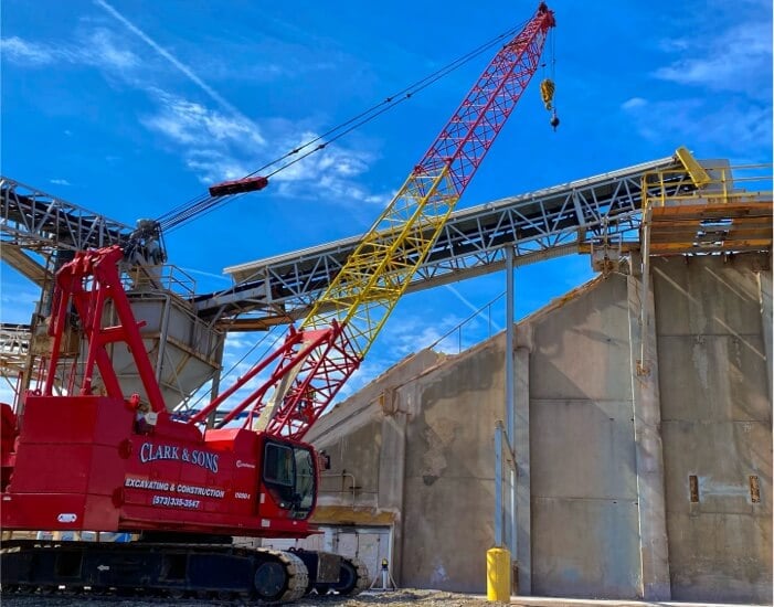 Red crane lifting materials at a construction site with the CLARK & SONS logo against a clear blue sky.