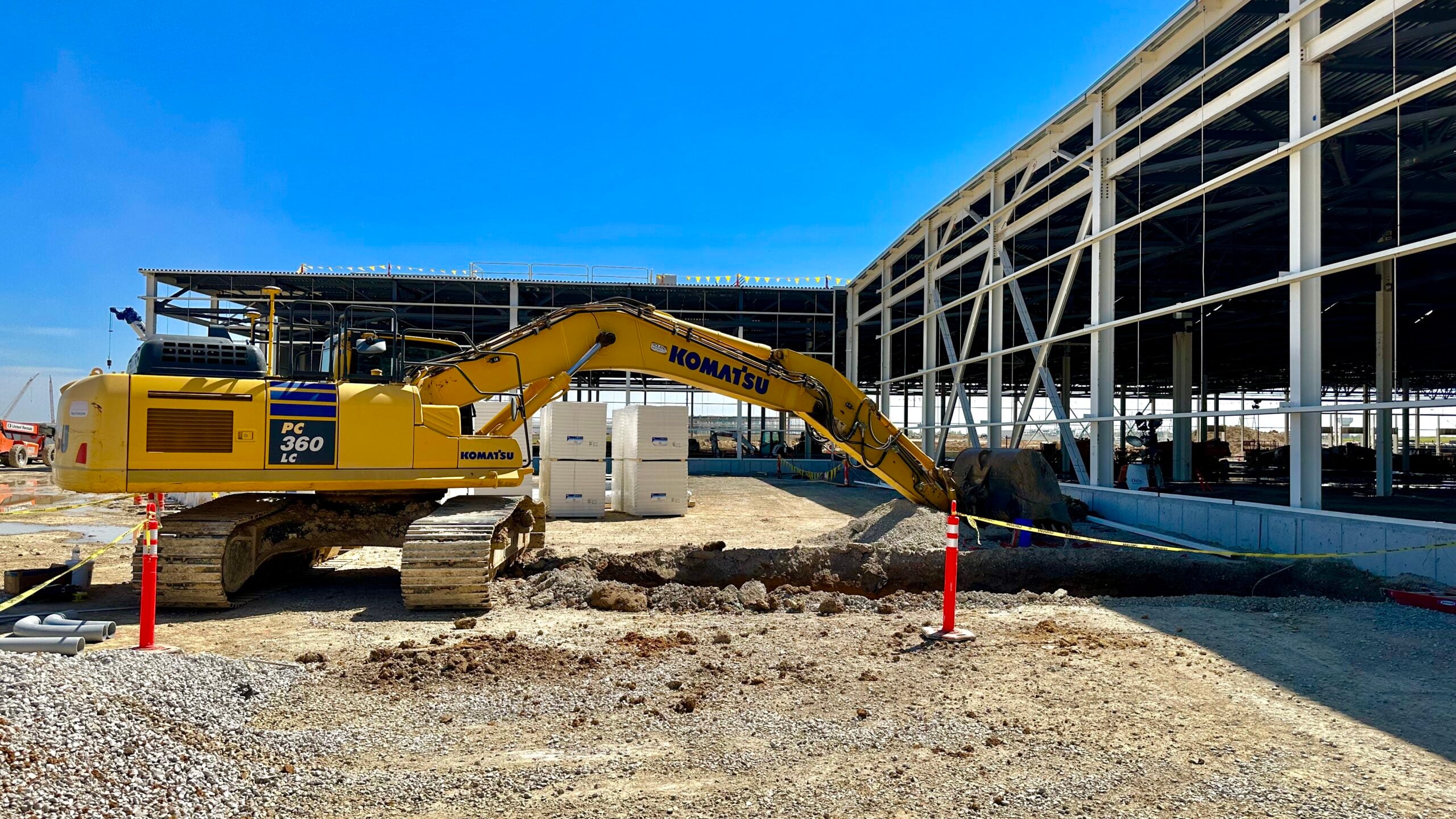 Komatsu excavator performing earthwork beside a steel-framed industrial building under construction.